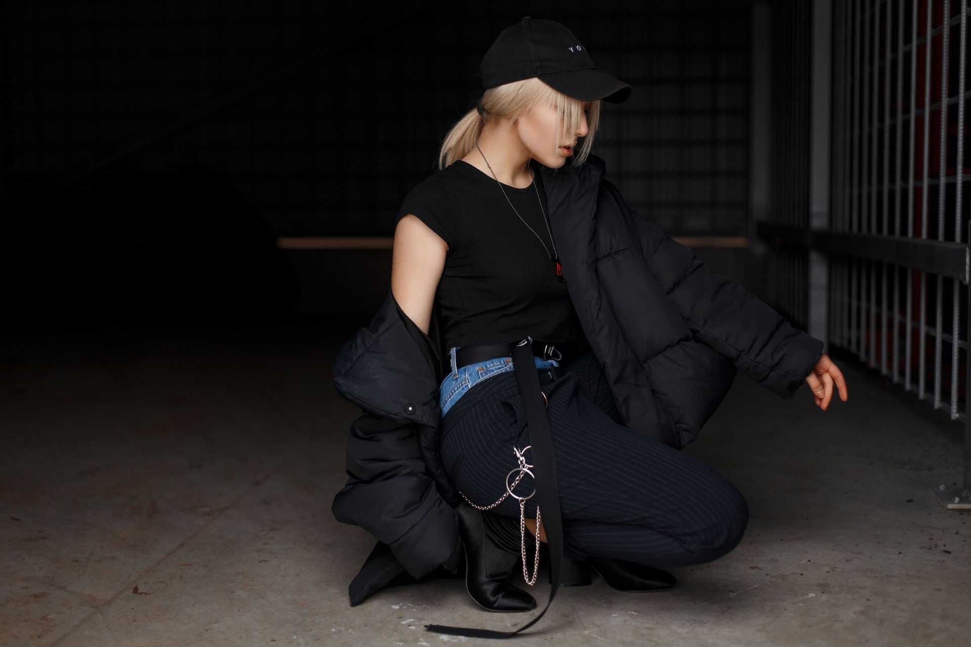 Stylish young model girl in a fashionable black winter jacket with a cap in fashionable pants with boots poses on a dark background